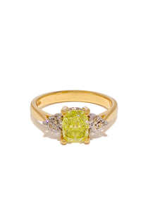 A Yellow diamond flanked by normal diamond trilogy ring in 18ct yellow gold lying on a white background